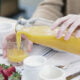 Cropped view of woman pouring orange juice from bottle into glass