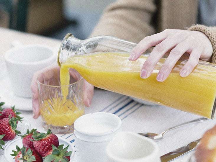 Cropped view of woman pouring orange juice from bottle into glass